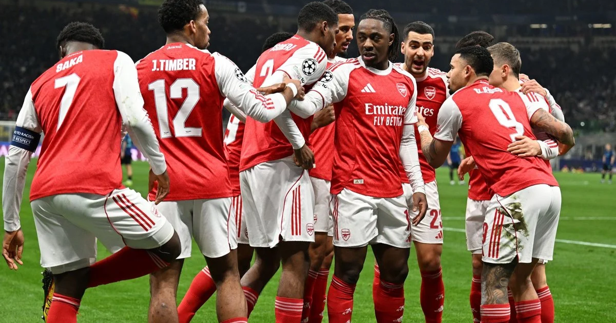 A group of Arsenal players, including Saka and Timber, huddling together in their red and white home kits on the pitch during a match.