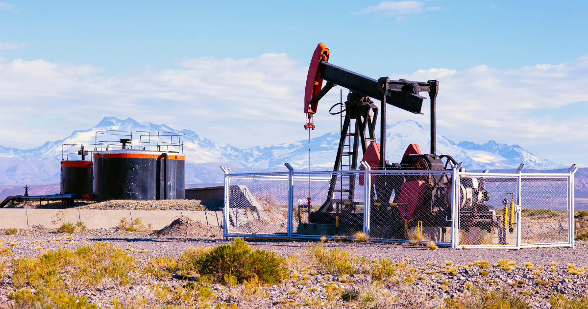 An oil pumpjack in a desert with snow-capped mountains in the distance.