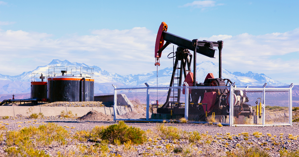 An oil pumpjack in a desert with snow-capped mountains in the distance.