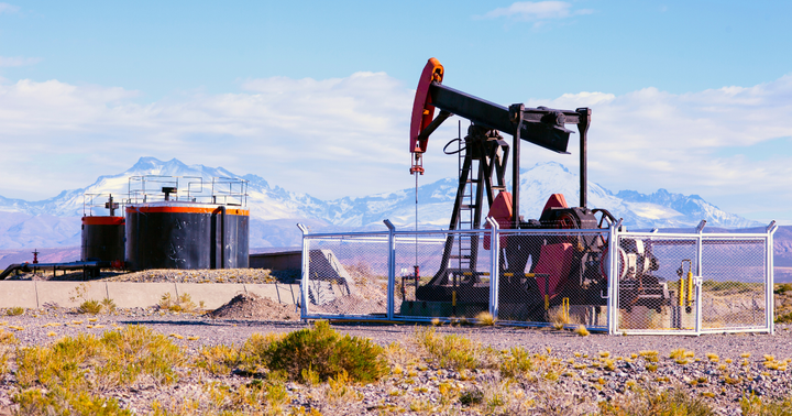An oil pumpjack in a desert with snow-capped mountains in the distance.